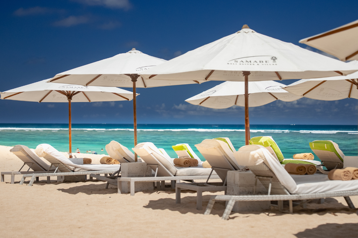 Shaded sunlounges on the beach at Samabe Bali Suites & Villas. Luxury Escapes.